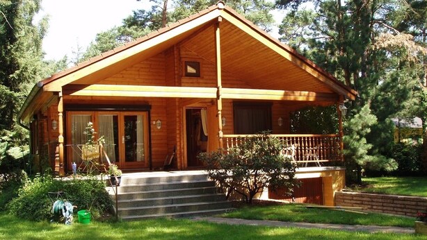 Une cabane en bois avec un porche, des marches menant à l’entrée et un petit jardin.