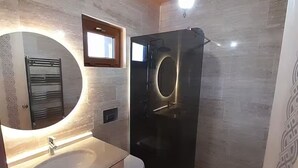Une salle de bain moderne avec un plafond en bois, un miroir rond, un lavabo, des toilettes et une douche à parois de verre.