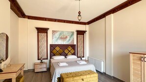 A bedroom with a wooden headboard, a bed with a patterned bedspread, a bedside table, a nightstand, a wooden bench, and a decorative ceiling light.