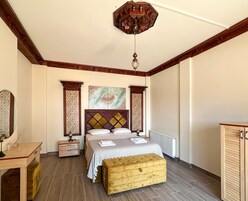 Un dormitorio con cabecera de madera, cama con colcha estampada, mesita de noche, banco de madera y una lámpara decorativa en el techo.