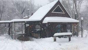 Een gebouw bedekt met sneeuw, met een puntig dak, een overdekte veranda en een bank ervoor.