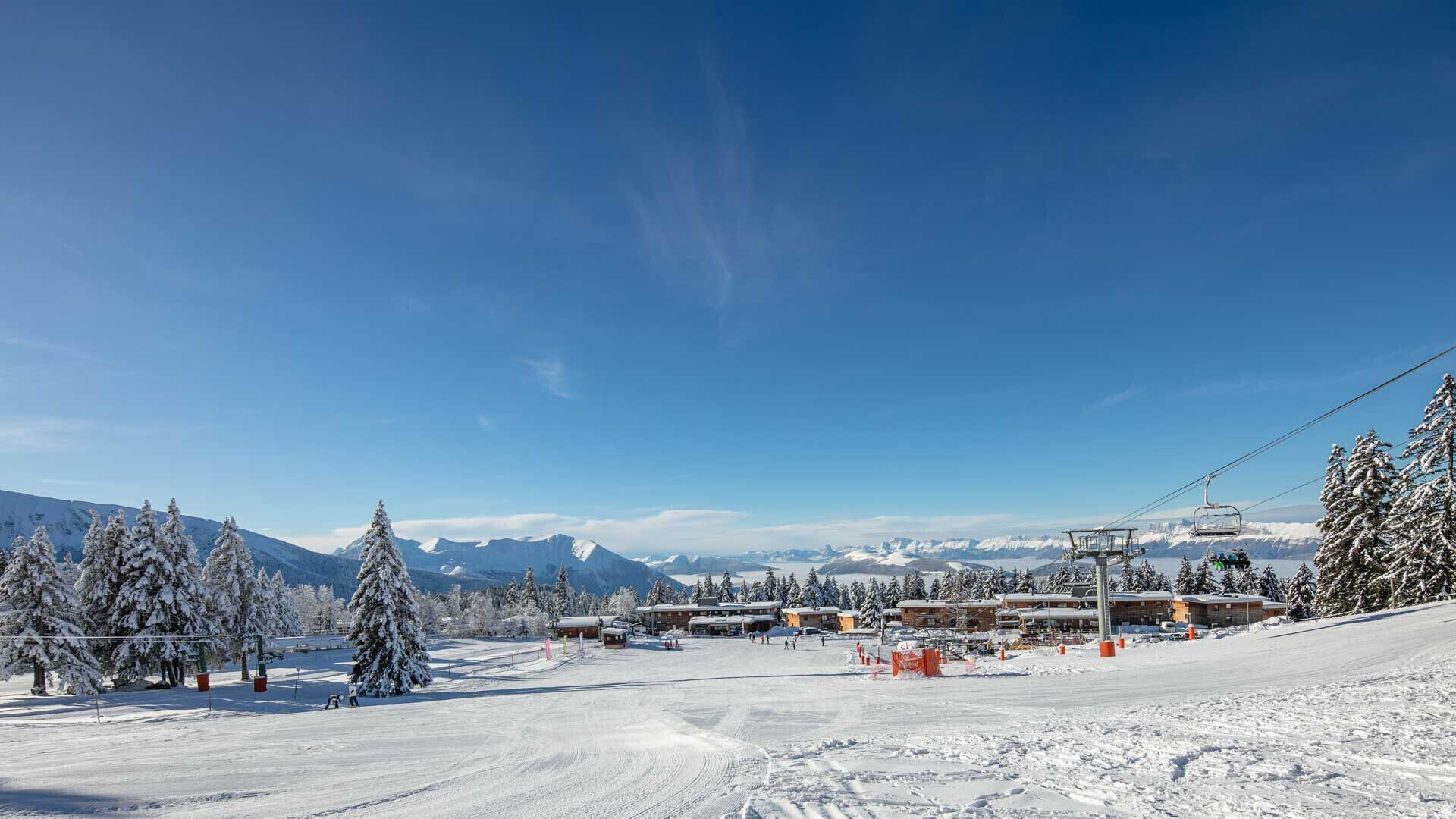 A snow-covered ski resort with a ski lift, buildings, and mountains in the background.