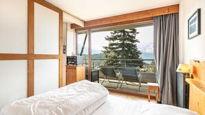 Ein Schlafzimmer mit einem großen Bett, einem Holztisch, einem Stuhl und einem Balkon mit Blick auf Bäume und Berge.