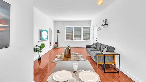 A modern living room with a sofa, a dining table set with plates and a coffee cup, a potted plant, and a wall-mounted TV. - Garden Suite 1-hosted by Sweetstay (Miami Beach)