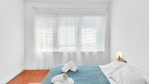A bedroom with a bed, a bedside table with a lamp, and a window with blinds. - Garden Suite 1-hosted by Sweetstay (Miami Beach)