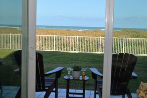 A patio with two chairs and a table, overlooking a beach and a white fence. - Cozy Oceanfront Condo with great ocean views! (South Padre Island)
