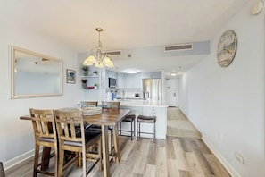 A modern kitchen with white cabinets, a central island, and a dining area with wooden chairs and a table. - Inviting oceanfront condo with balcony, pool, hot tub, sauna, & W/D (Myrtle Beach)