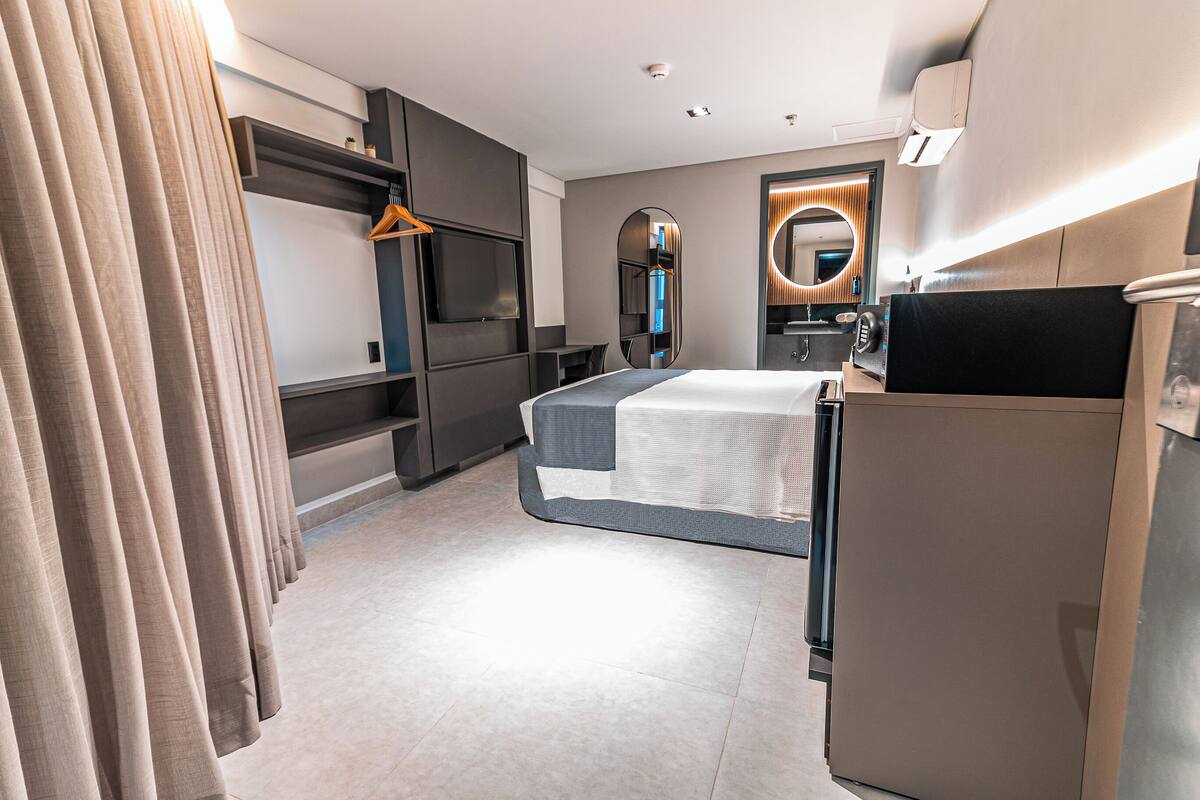 Ein modernes Hotelzimmer mit Bett, Fernseher, Spiegel und Minibar.
