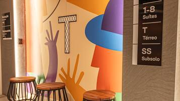 A hotel interior with a colorful wall design, three wooden stools, and a sign indicating room types.