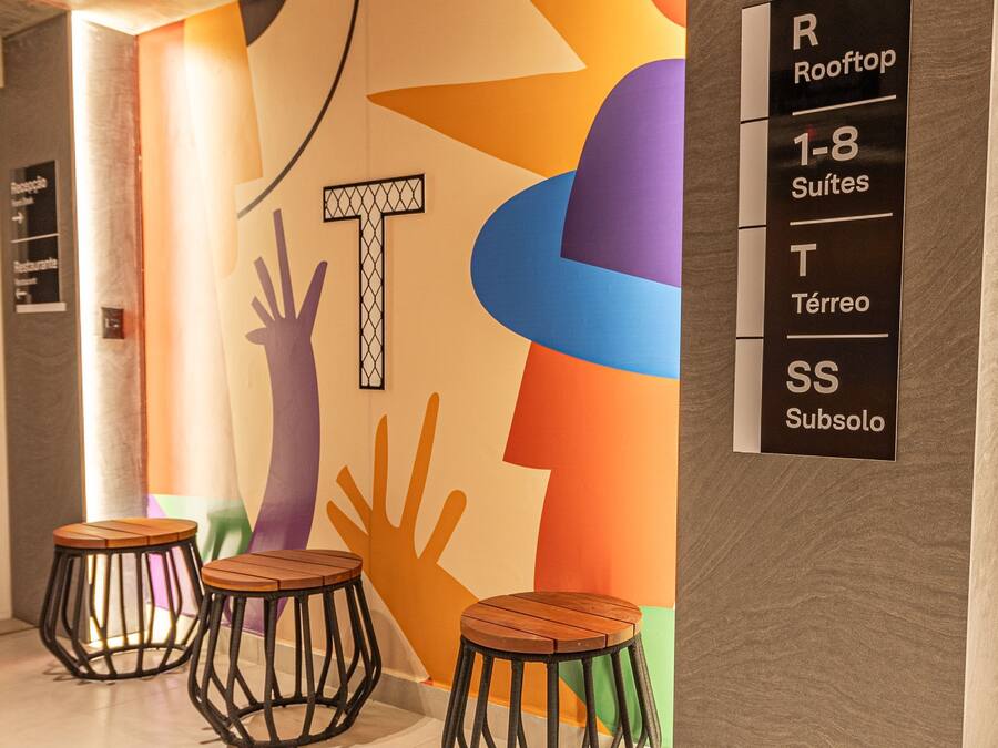 A hotel interior with a colorful wall design, three wooden stools, and a sign indicating room types.