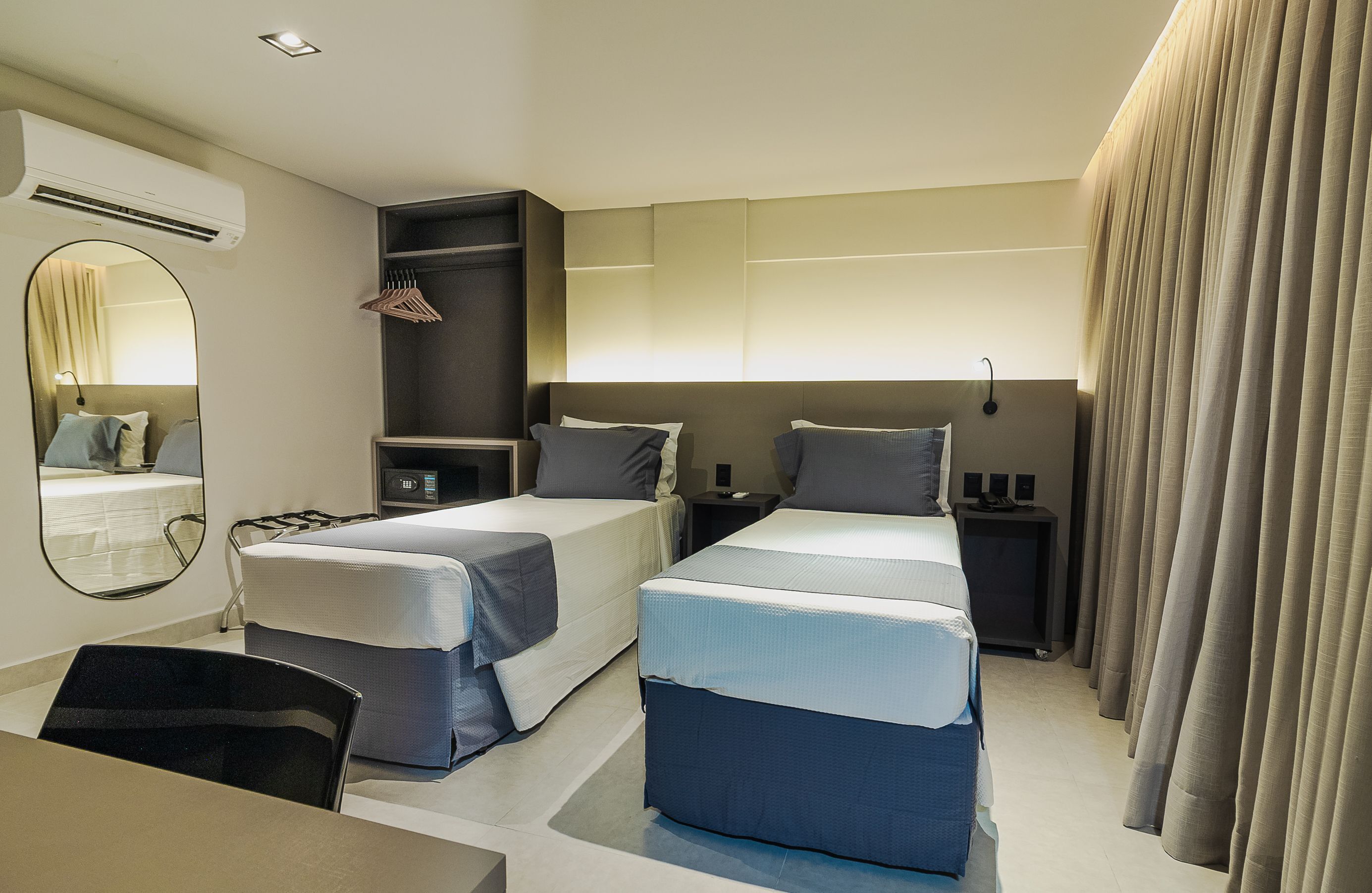 Une chambre d’hôtel moderne équipée de deux lits, d’un bureau, d’une chaise, d’un miroir, d’une armoire et d’un rideau.