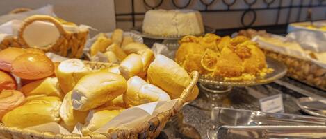 A buffet with various food items including rolls, sandwiches, and pastries.