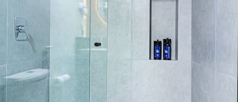 A modern bathroom with a glass shower enclosure, a toilet, and a shelf with toiletries.