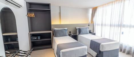 A hotel room with two beds, a desk, a chair, and a wardrobe.