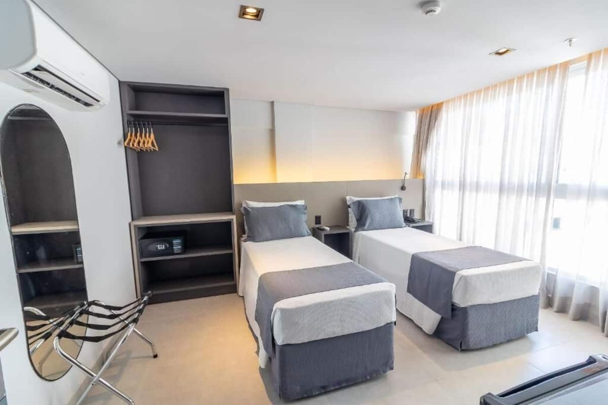 Ein Hotelzimmer mit zwei Betten, einem Schreibtisch, einem Stuhl und einem großen Fenster mit Vorhängen.
