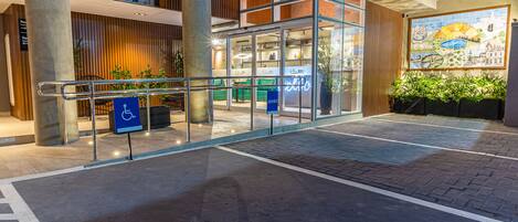A hotel entrance with a glass facade, a wheelchair-accessible sign, and a mural on the wall.