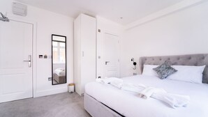 A hotel room with a large bed, white bedding, a grey headboard, a mirror, and a small trash bin. - The Woodman Hotel (London)