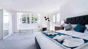 A modern bedroom with a large bed, a bedside table, a mirror, and a window with a view of trees. - The Woodman Hotel (London)