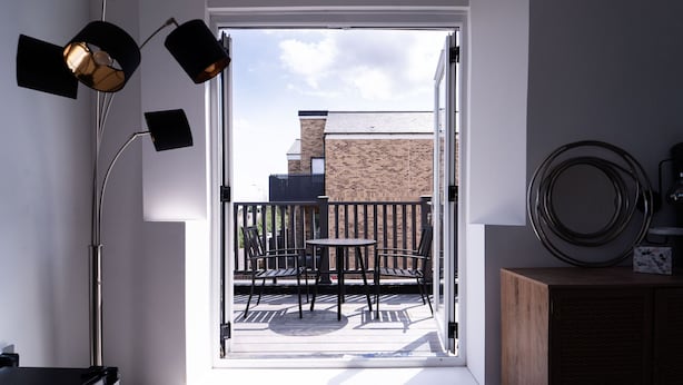 A room with a sliding glass door leading to an outdoor patio with a table and chairs, a modern floor lamp, and a wooden cabinet. - The Woodman Hotel (London)