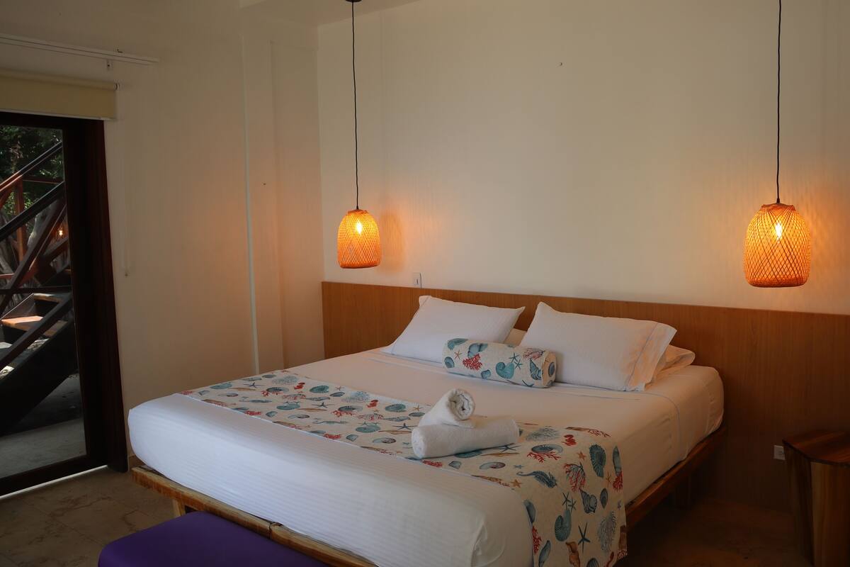 Una cama bien hecha con una colcha estampada y almohadas, dos lámparas colgantes y un cabecero de madera.
