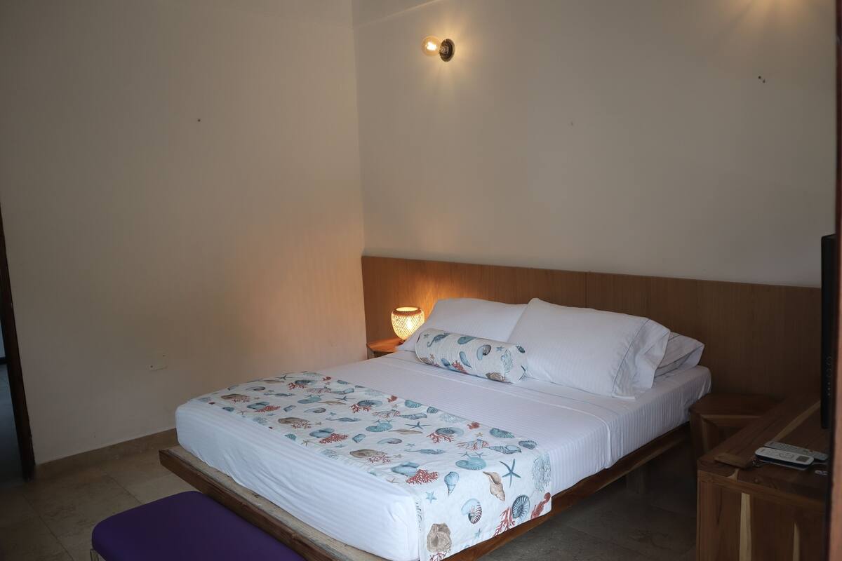 Una cama bien hecha con una colcha estampada con motivos florales, un cabecero de madera y una lámpara de noche.