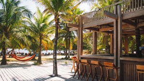 Una terraza de madera con taburetes y una zona de bar, rodeada de palmeras.