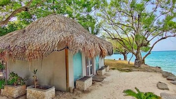 Eine Reetdachhütte mit Blick aufs Meer, umgeben von Bäumen und Pflanzen.