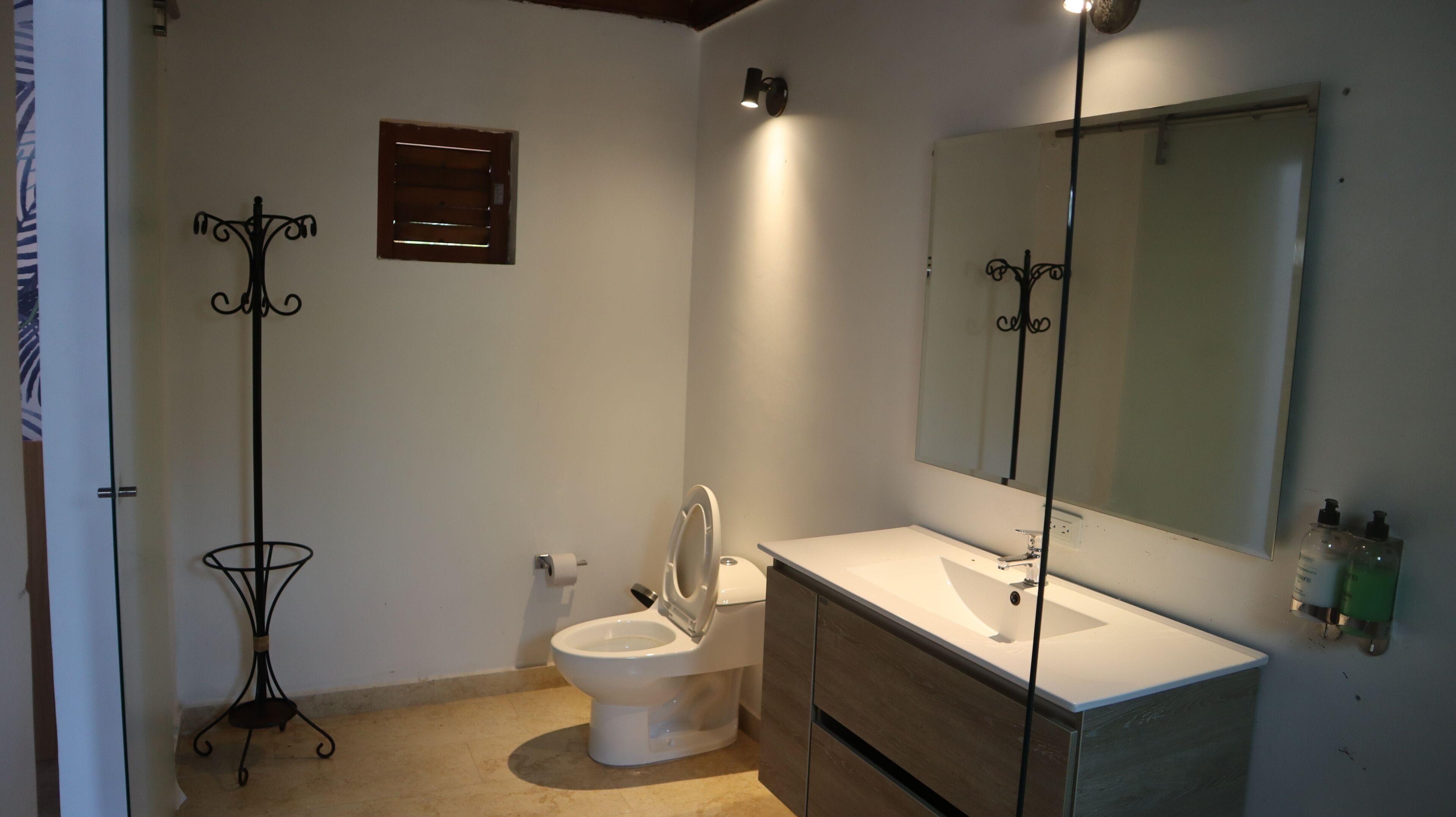 Un baño con inodoro, lavamanos, espejo y una ventana pequeña.