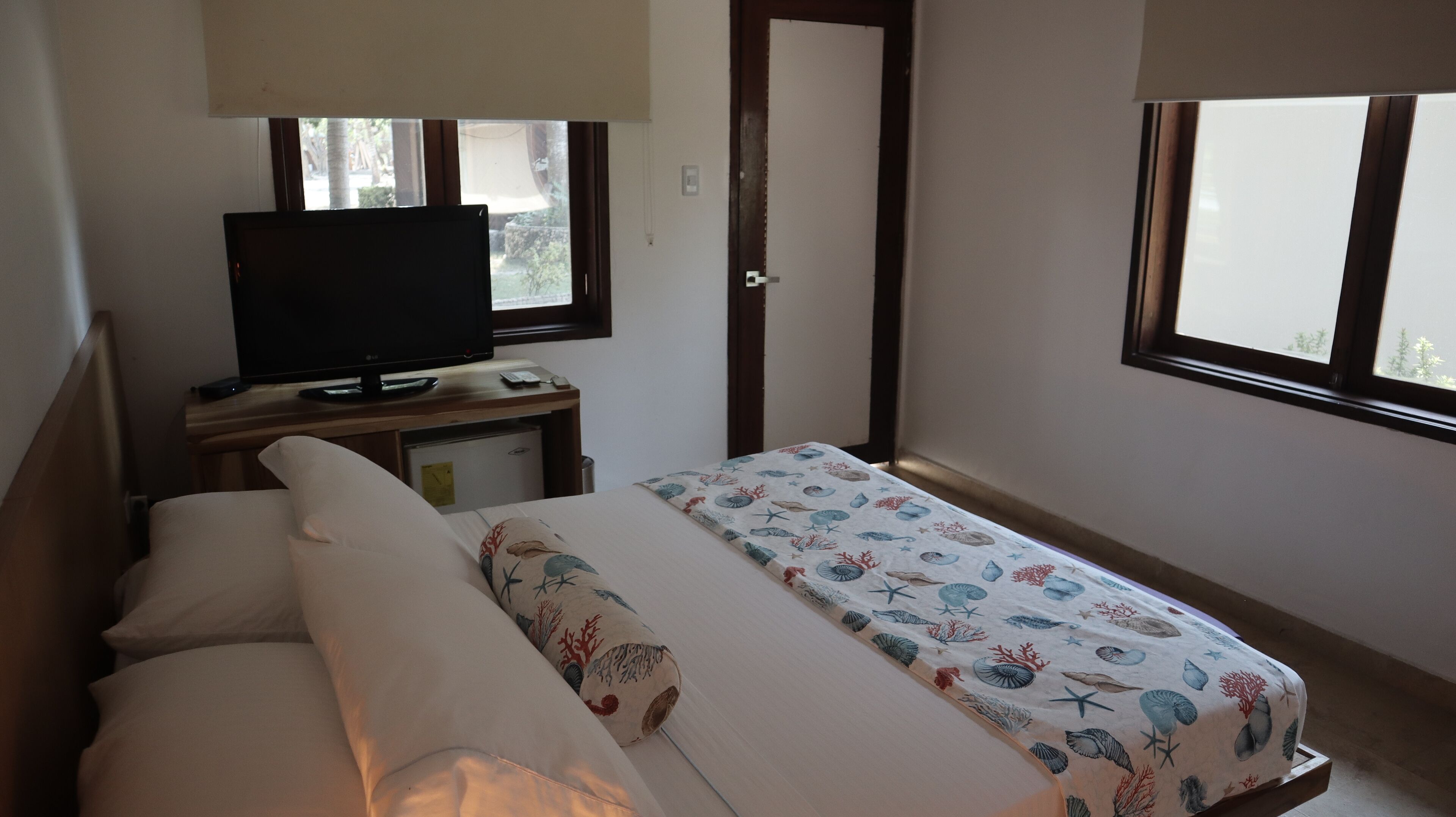 Un dormitorio con una cama, un escritorio con televisor y una ventana.