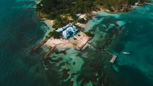 Vista aérea de una isla tropical con una casa grande rodeada de aguas turquesas cristalinas.