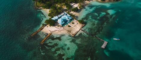 An aerial view of a tropical island with a large house surrounded by clear turquoise waters.