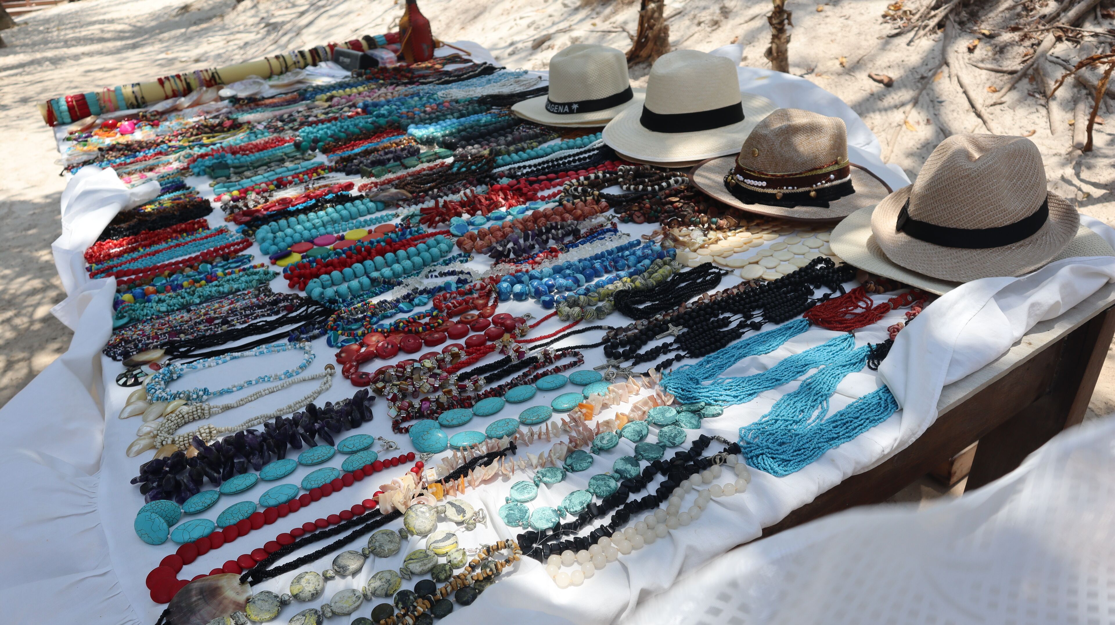 A variety of colorful necklaces and hats displayed on a table outdoors.