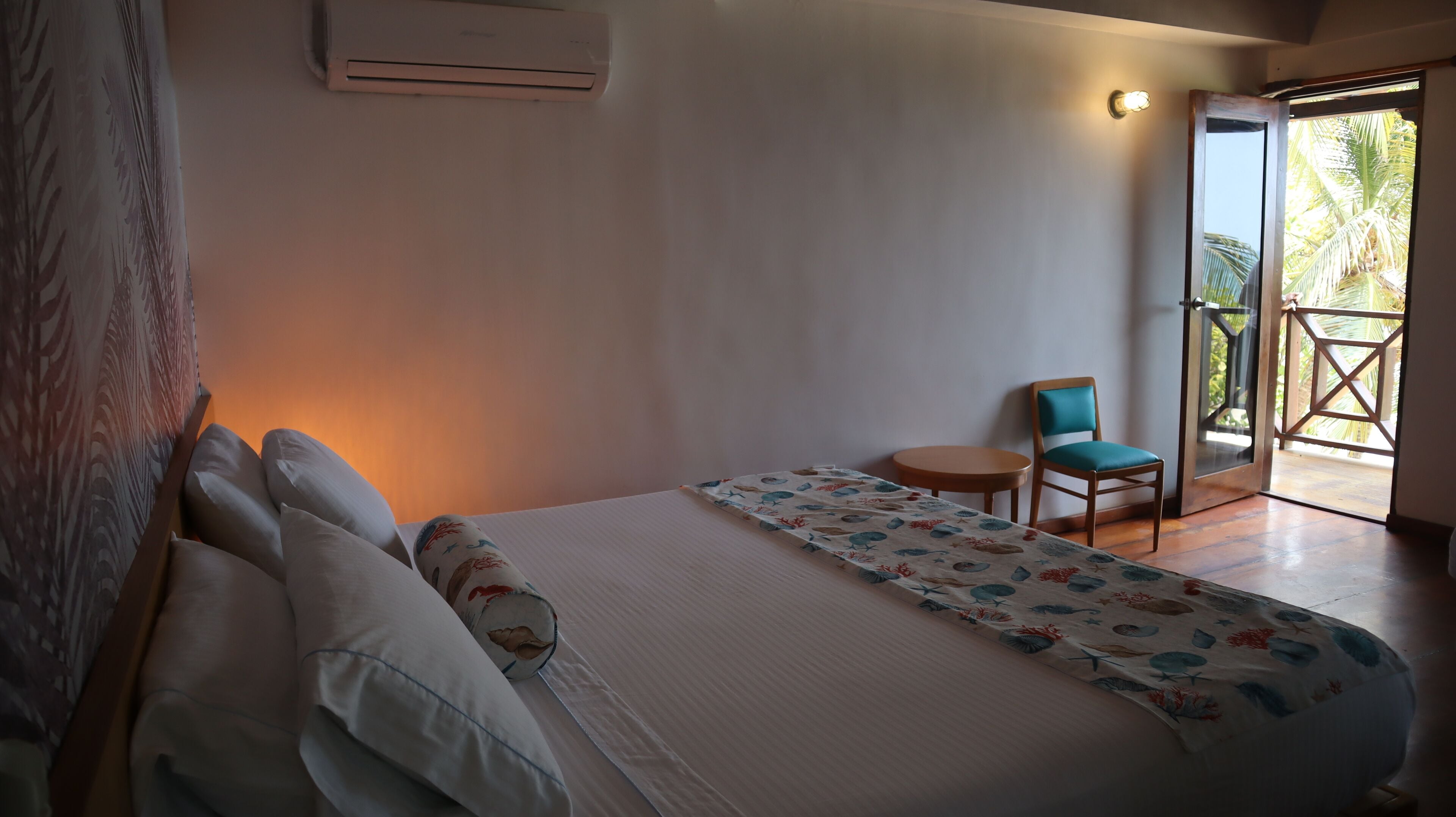 Ein Schlafzimmer mit Bett, Kissen, einem kleinen Tisch, einem Stuhl und Blick ins Freie.