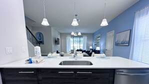 A modern kitchen with a white countertop, dark wood cabinets, a stainless steel sink, and pendant lighting. - Balmoral Resort-213al 3 Bedroom Home by RedAwning (Haines City)