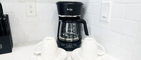 A black Mr. Coffee coffee maker on a white countertop with two white cups and saucers.