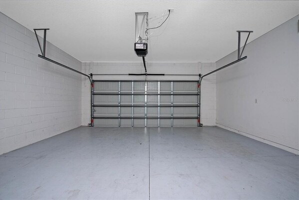 A garage with a closed garage door, white brick walls, and a concrete floor.