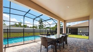 A covered patio with a glass enclosure, a pool, and a dining area with wicker furniture. - Balmoral Resort-224mcv 4 Bedroom Home by RedAwning (Haines City)