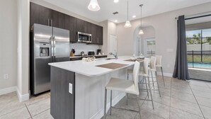 A modern kitchen with a central island, stainless steel appliances, and a dining area with bar stools. - Balmoral Resort-224mcv 4 Bedroom Home by RedAwning (Haines City)