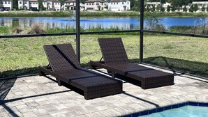 A poolside area with two lounge chairs and a view of a lake and houses in the background. - Balmoral Resort-210bp 4 Bedroom Home by RedAwning (Haines City)
