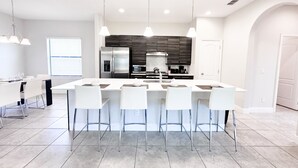 A modern kitchen with a central island, bar stools, stainless steel appliances, and pendant lighting. - Balmoral Resort-210bp 4 Bedroom Home by RedAwning (Haines City)