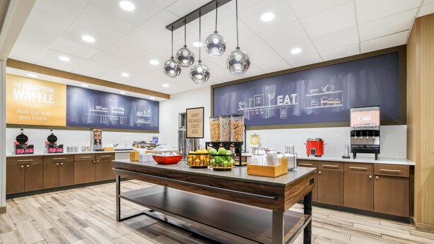 A modern kitchen area with a breakfast bar, fruit display, and a chalkboard menu. - Hampton Inn Fort Myers Downtown (Fort Myers)