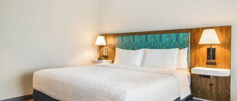 Een hotelkamer met een groot bed, twee nachtkastjes met lampen, een houten hoofdbord en een inbouwplank.