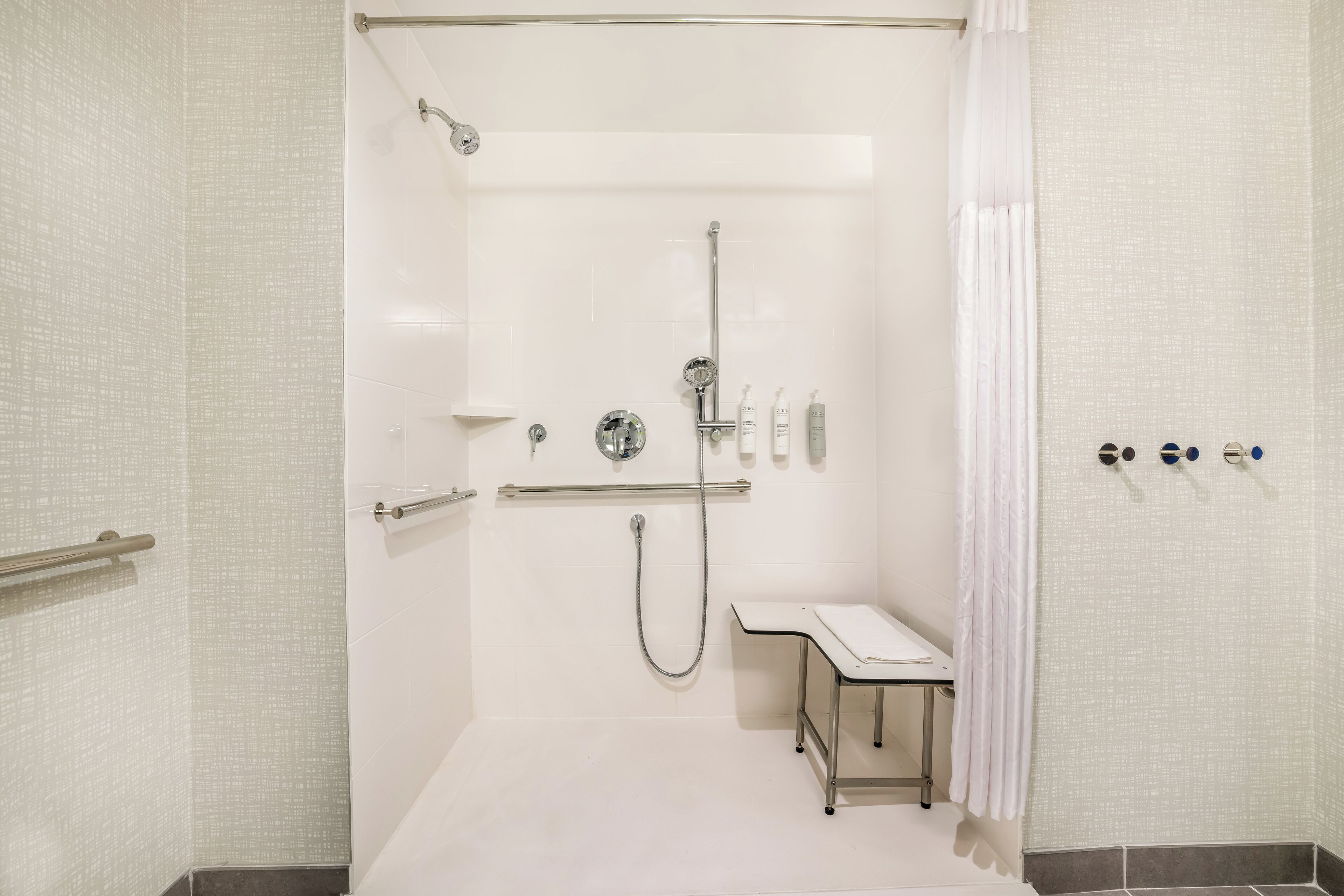 Un espace douche moderne doté d’une paroi en verre, d’une barre d’appui, d’un banc et d’un ensemble de produits de toilette.