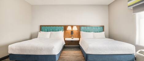 A hotel room with two beds, a wooden headboard, a small sink, and a window with a view.