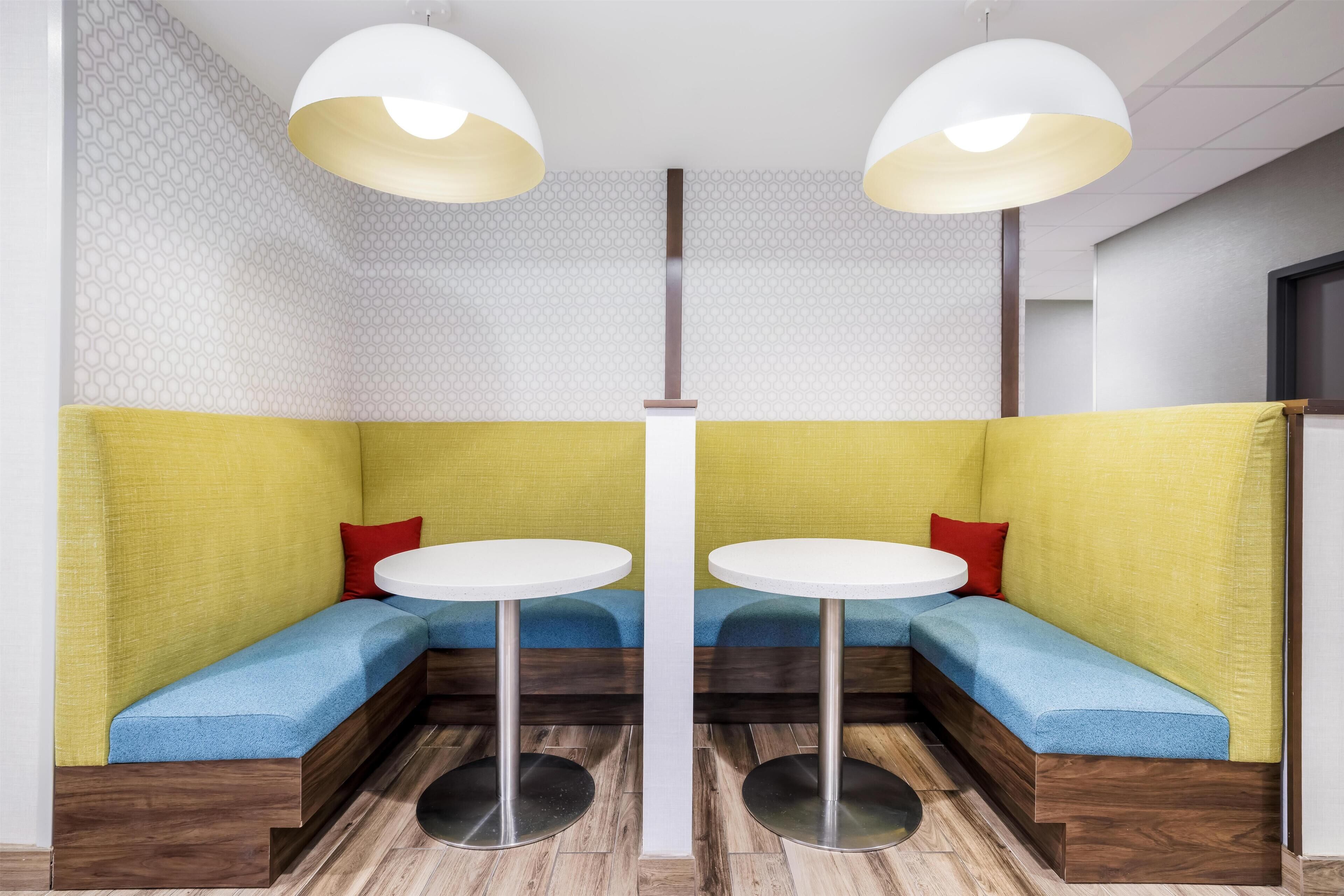 Un espacio de descanso con dos mesas redondas, bancos acolchados e iluminación colgante.