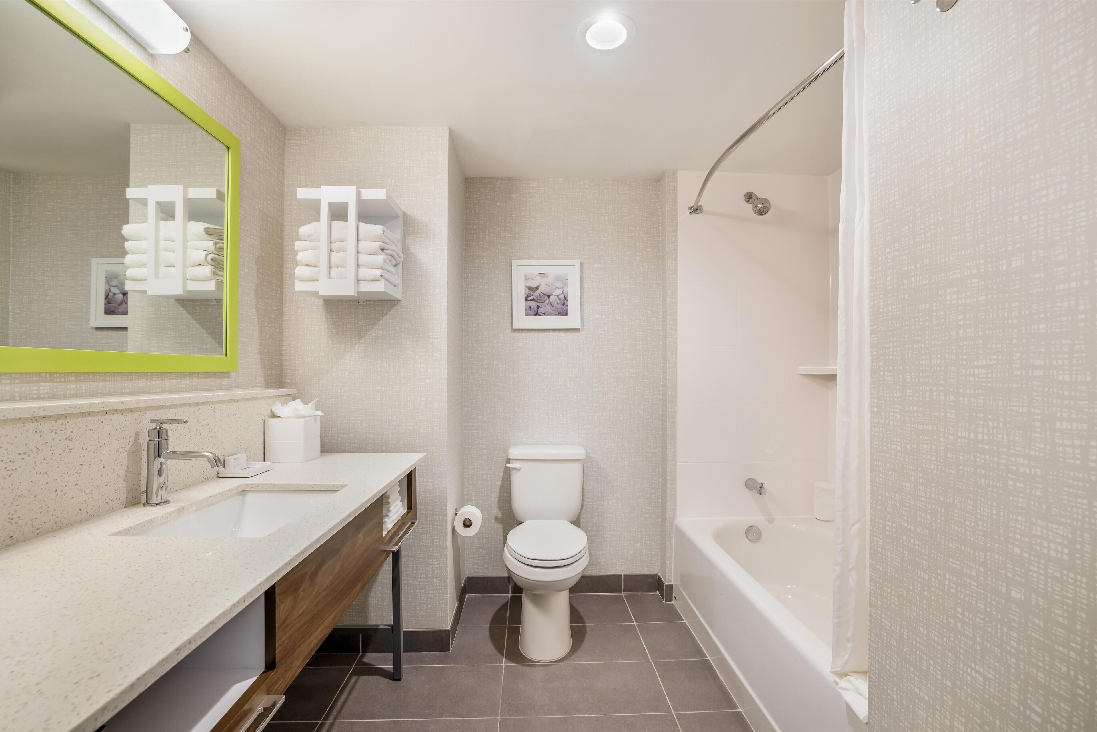 A modern bathroom with a white sink, mirror, and toilet. There is a shower area with a glass door and a bathtub.