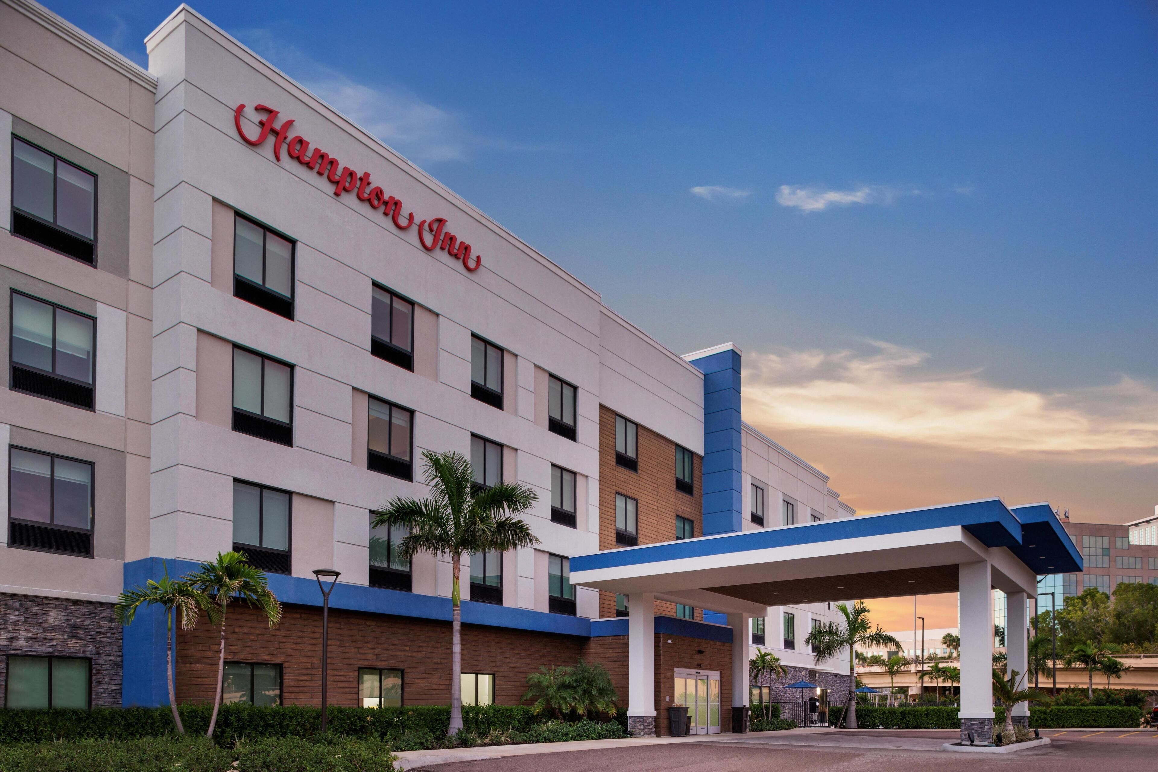 A Hampton Inn hotel with a modern facade, multiple floors, and a covered outdoor area with a blue roof.
