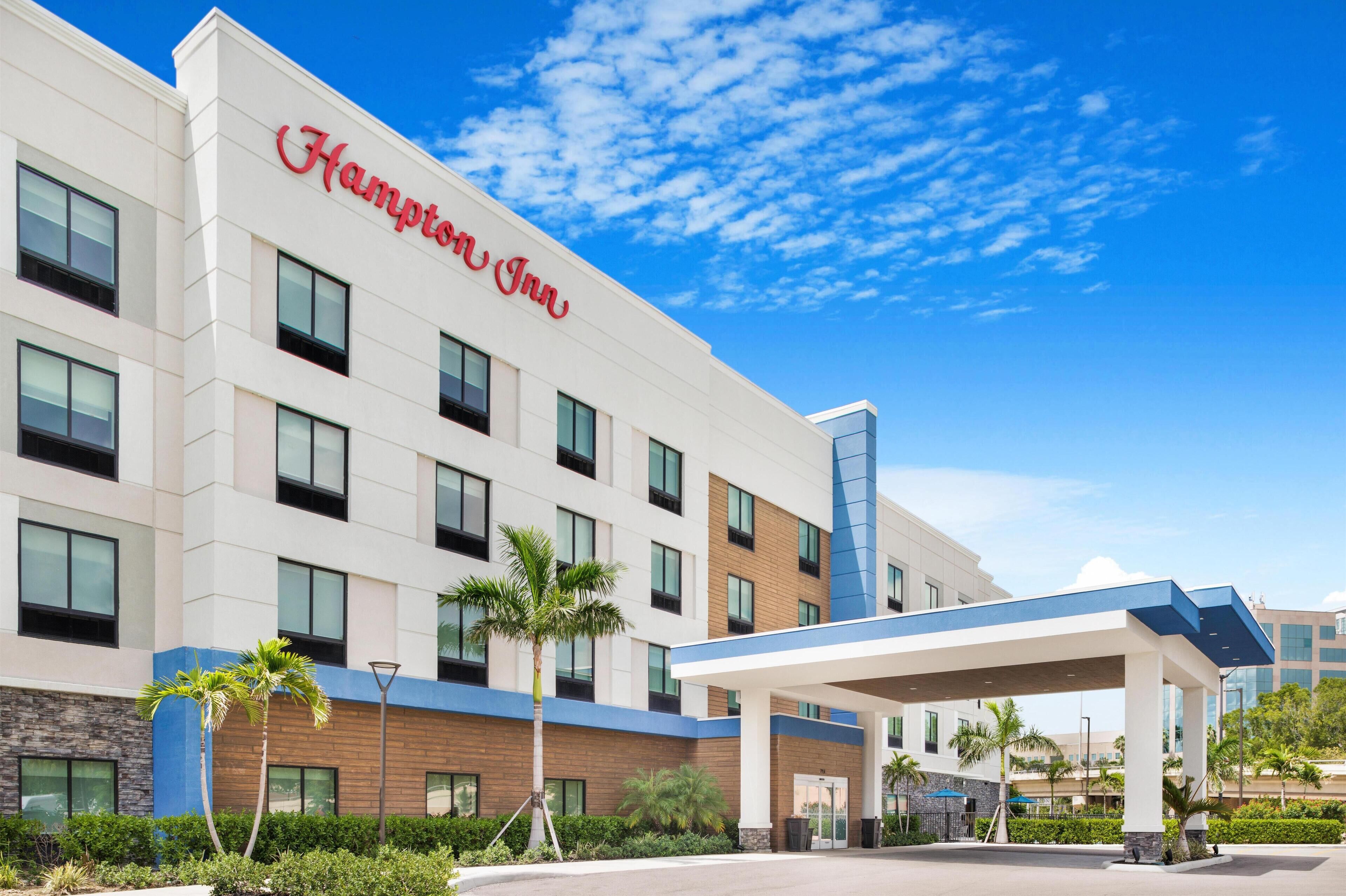 Um hotel Hampton Inn com design moderno, apresentando uma entrada destacada e uma área externa coberta.