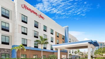 Um hotel Hampton Inn com design moderno, apresentando uma entrada destacada e uma área externa coberta.