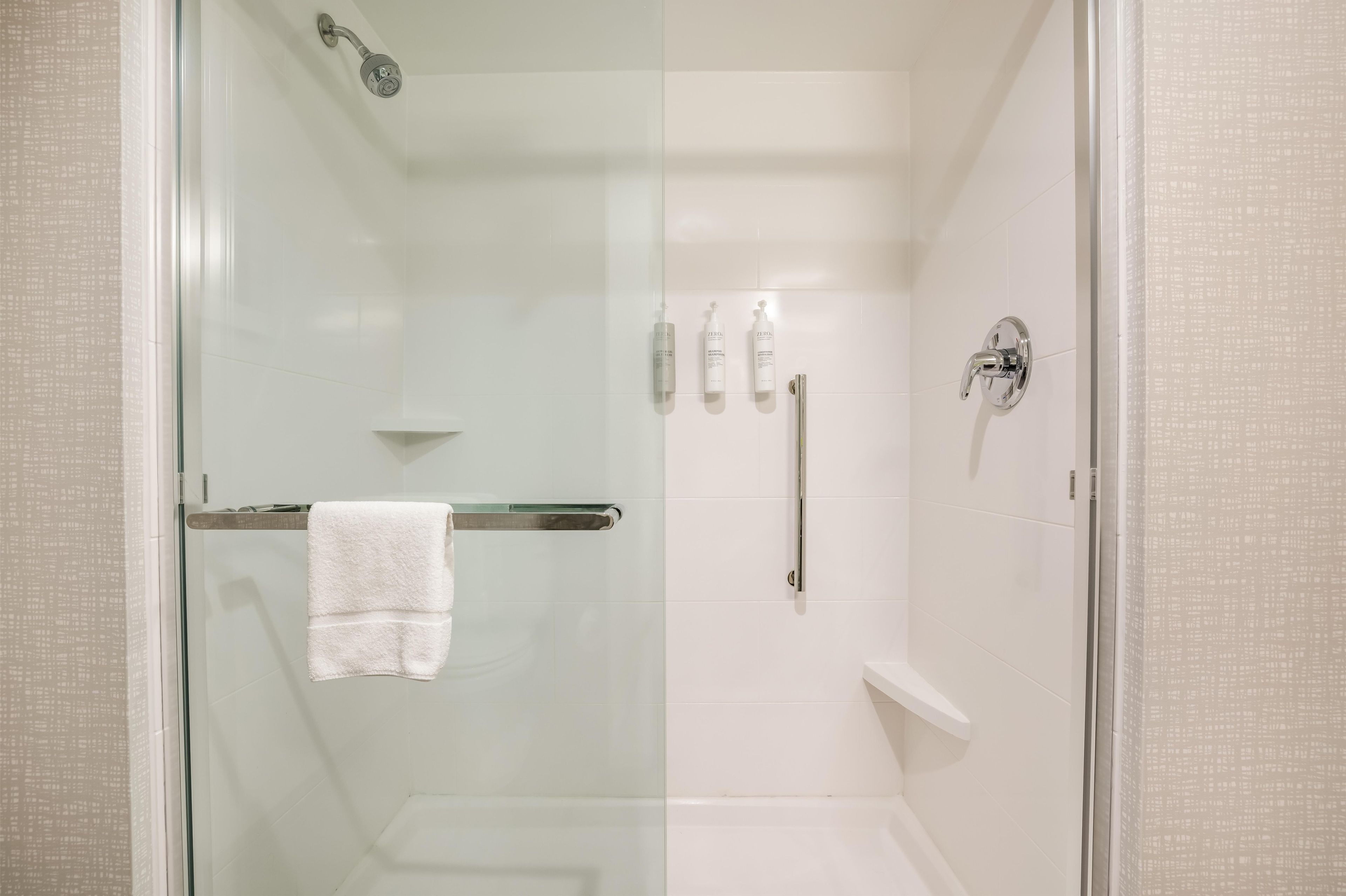A glass-enclosed shower area with a white towel on a metal rack, a glass shower door, and a white tiled wall.